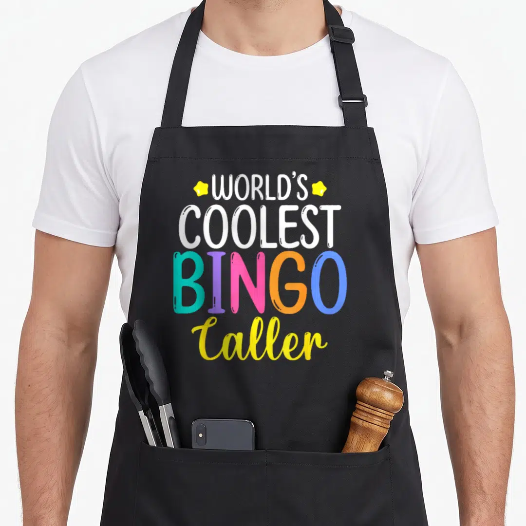 Player coolest bingo aprons - Stacked text reading World's Coolest Bingo Caller with multi-colored letters and yellow — shown on a black cotton canvas apron against a white background