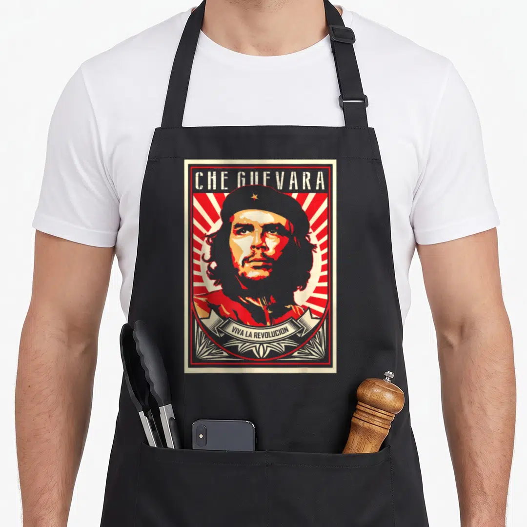 Che novelty apron - Che Guevara portrait with Viva La Revolucion banner on red white sunburst background — shown on a black cotton canvas apron against a white background