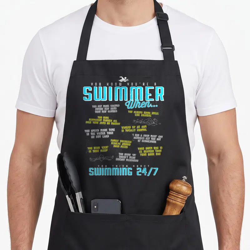List swimmer apron - Swimmer list text with white gear silhouettes in blue yellow and white on black — shown on a black cotton canvas apron against a white background