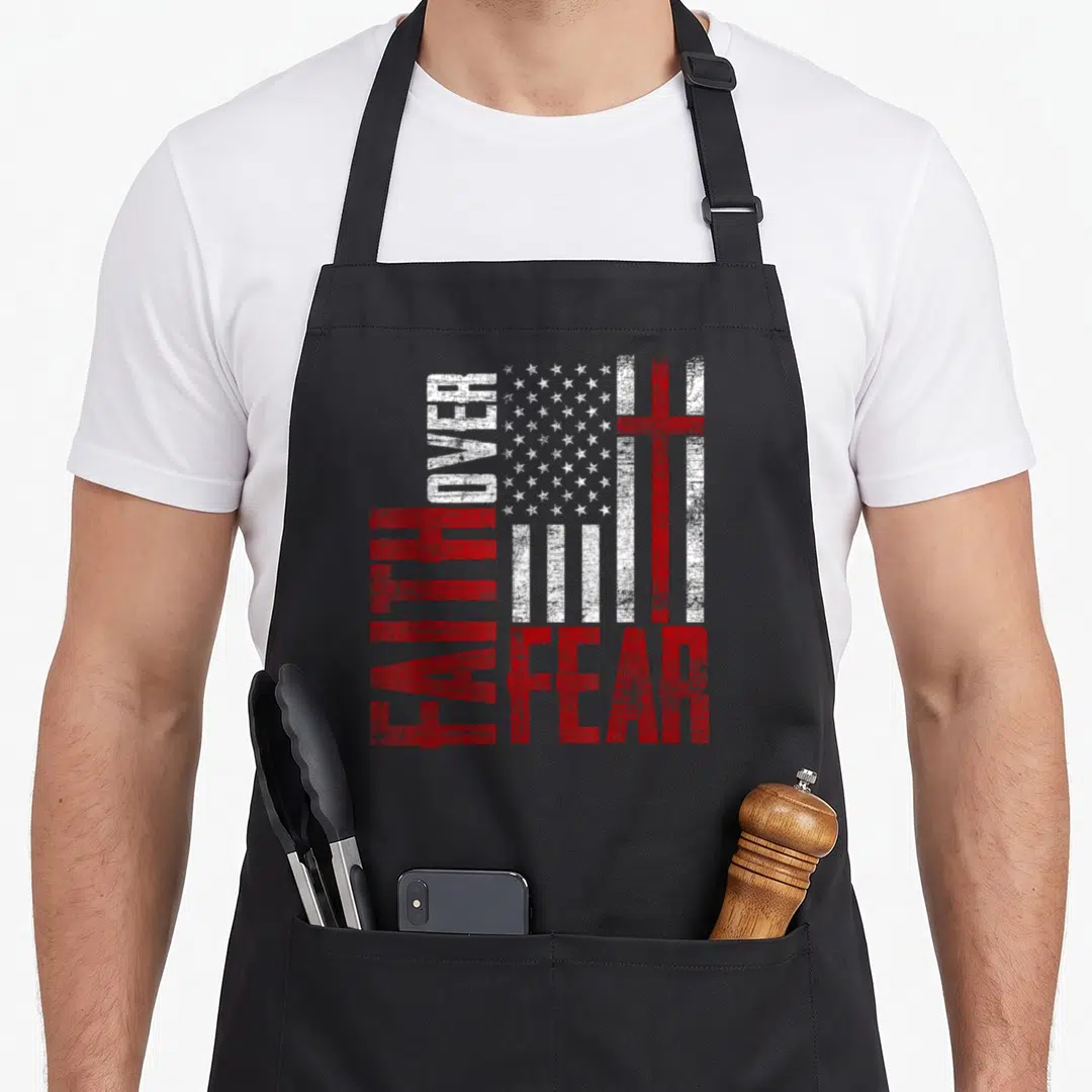 Patriotic cross over apron - Distressed USA flag with FAITH OVER FEAR text and red cross in red and white — shown on a black cotton canvas apron against a white background