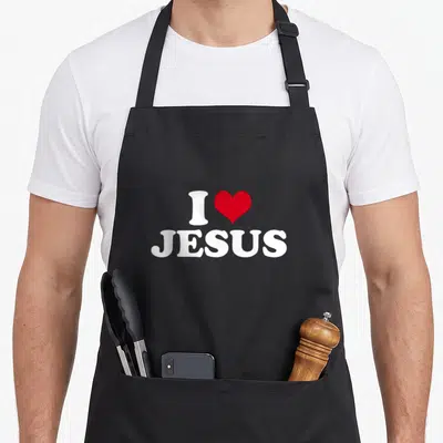 Funny jesus apron - White I and JESUS text with red heart symbol — shown on a black cotton canvas apron against a white background