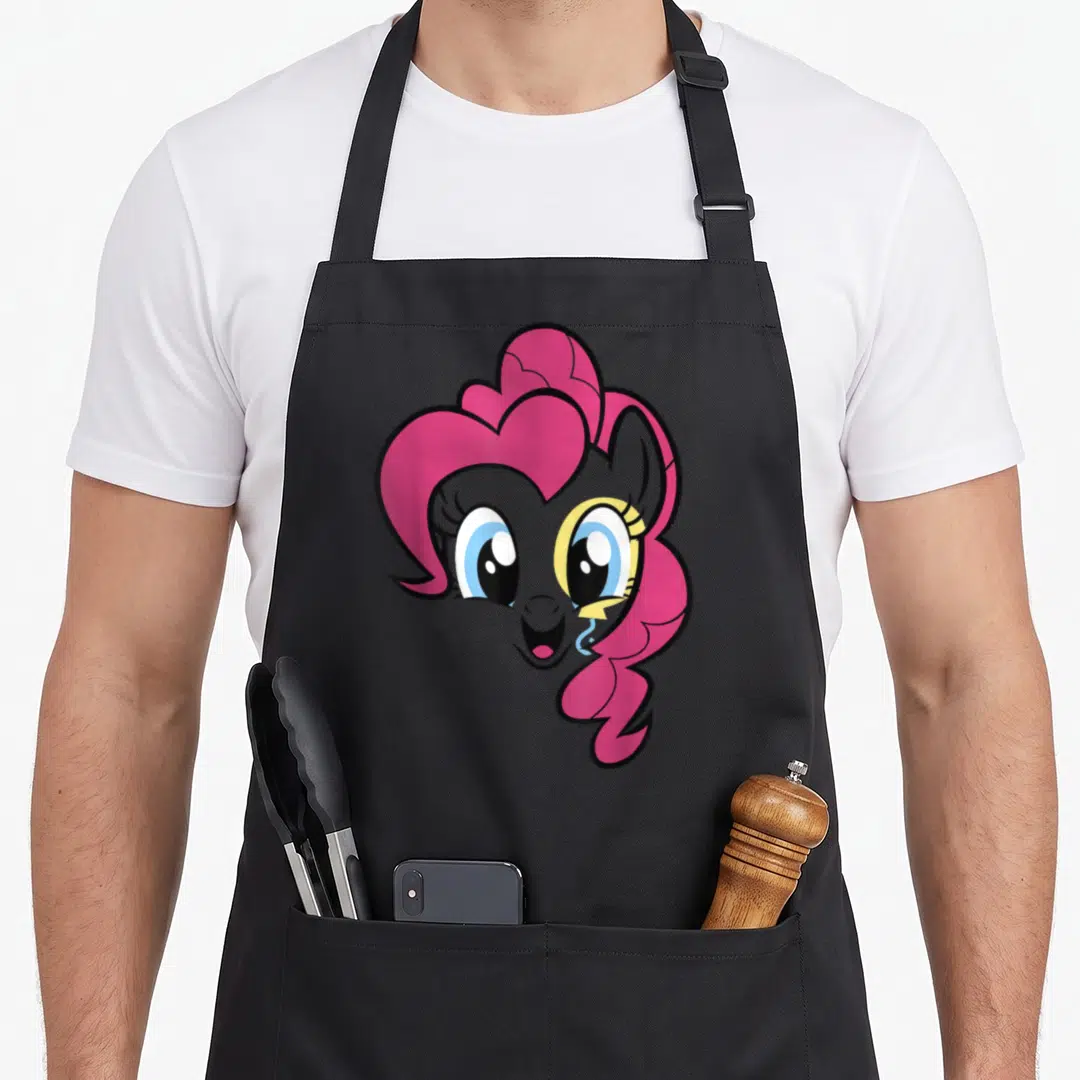 Magic pie apron - Cartoon pony head with pink mane, grey face, blue eyes, and yellow accent — shown on a black cotton canvas apron against a white background