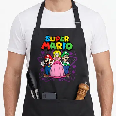 Trio peach apron - Super Mario, Peach, and Luigi in front of purple star with hearts and colorful text — shown on a black cotton canvas apron against a white background