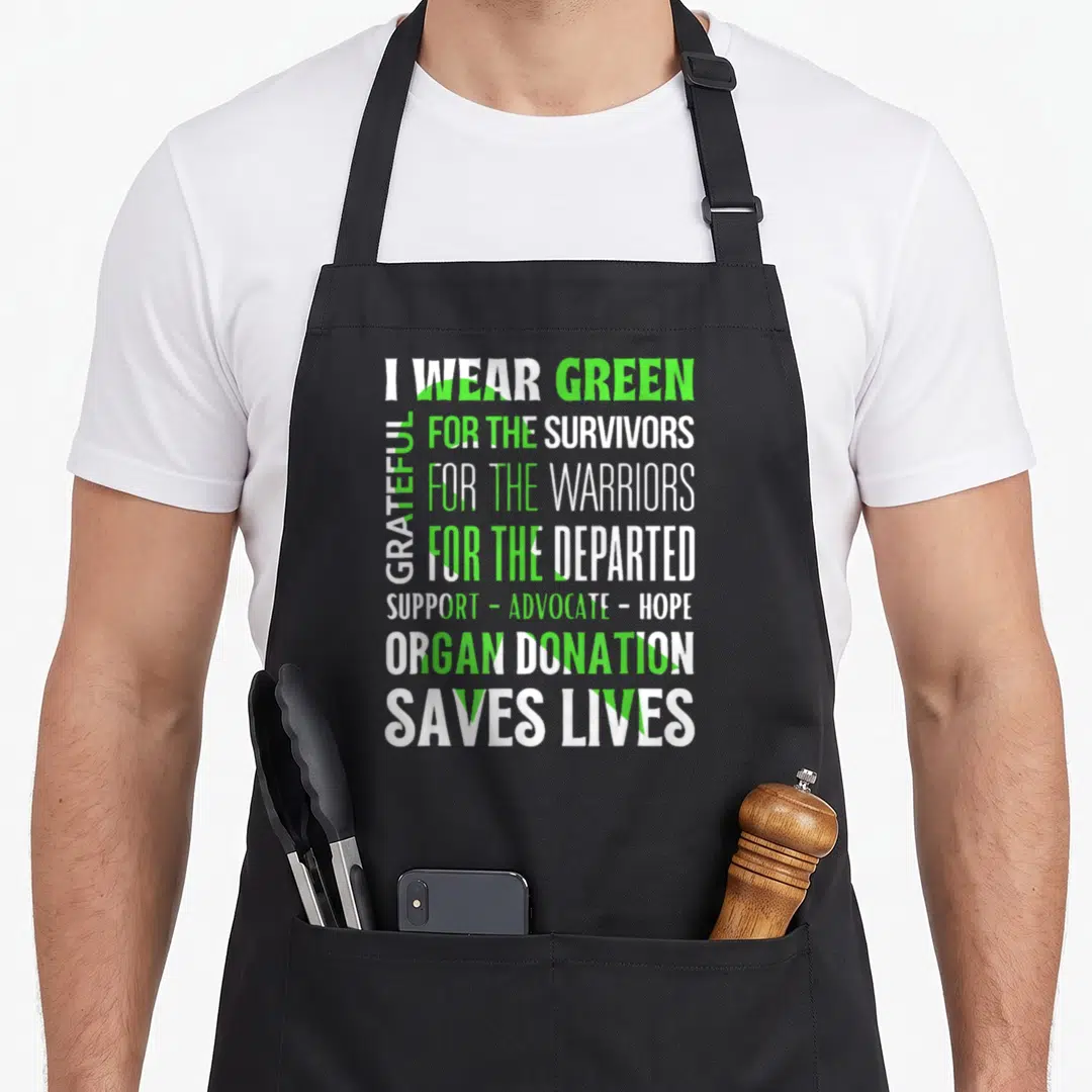 Modern organ apron - Stacked I WEAR GREEN text over a green awareness ribbon representing organ donation support — shown on a black cotton canvas apron against a white background