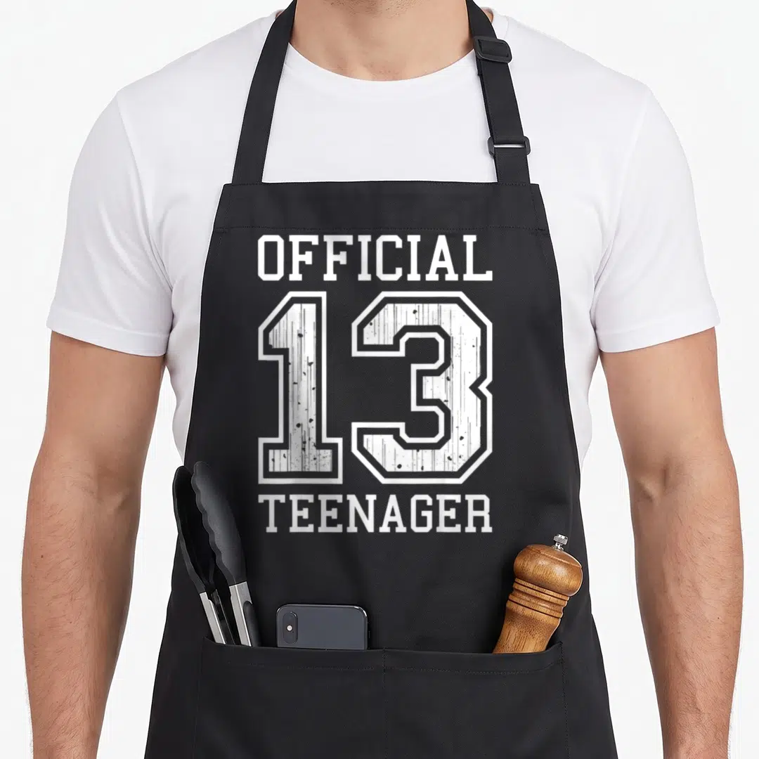 Vintage 13th birthday apron - White text reading Official 13 Teenager stacked vertically on grey background — shown on a black cotton canvas apron against a white background