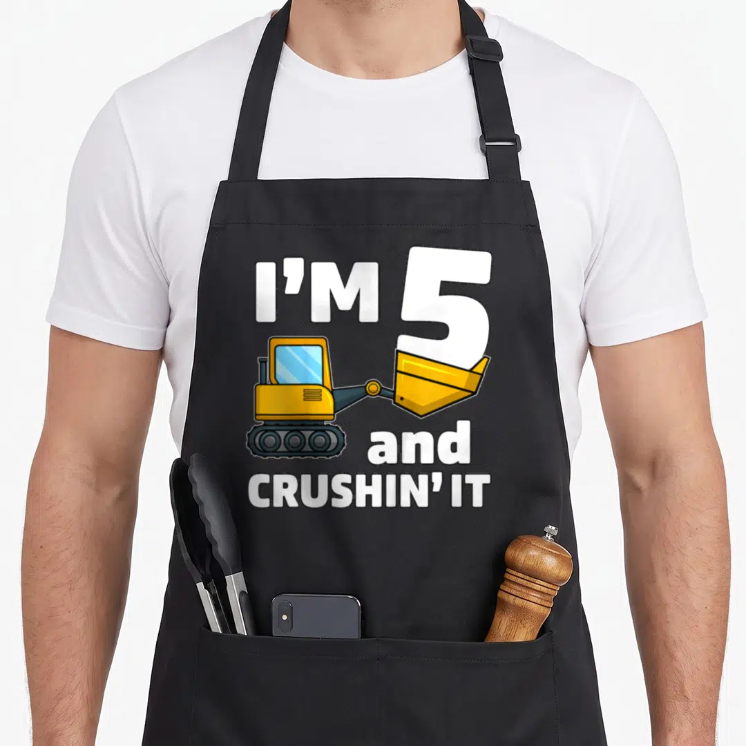 Construction 5th truck apron - Cartoon excavator lifting number 5 with text I'm 5 and crushing it — shown on a black cotton canvas apron against a white background