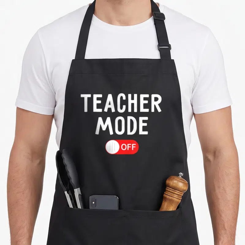 Mode school teacher apron - Stacked white text reading TEACHER MODE above a red toggle switch set to OFF — shown on a black cotton canvas apron against a white background