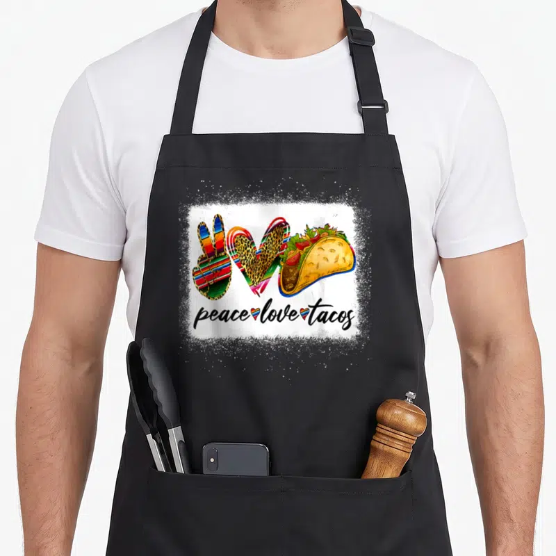 Peace mexican apron - Peace sign heart and taco illustration above peace love tacos text — shown on a black cotton canvas apron against a white background