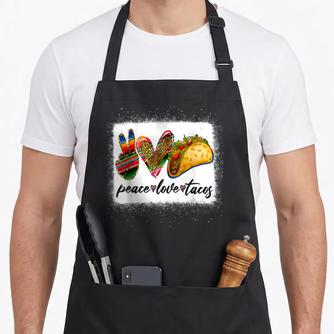 Peace mexican apron - Peace sign heart and taco illustration above peace love tacos text — shown on a black cotton canvas apron against a white background