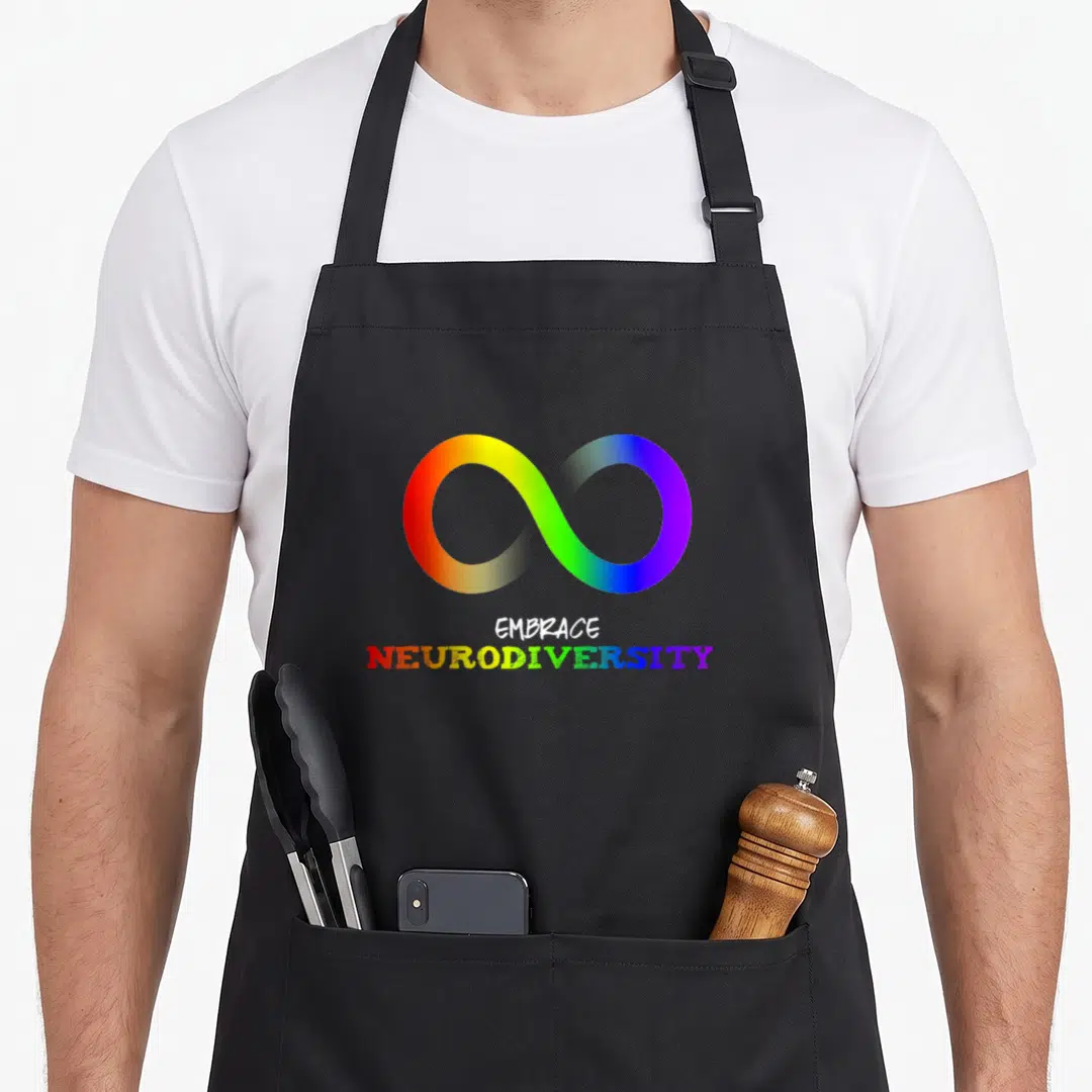 Asd rainbow apron - Rainbow infinity symbol above EMBRACE NEURODIVERSITY text in white and rainbow colors — shown on a black cotton canvas apron against a white background