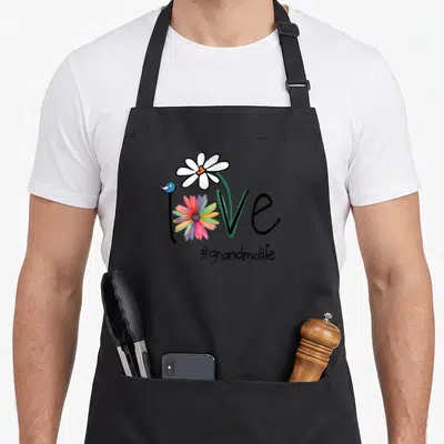 Flower grandma apron - Love word with multicolored flower o, white daisy, blue bird, #grandmalife text — shown on a black cotton canvas apron against a white background