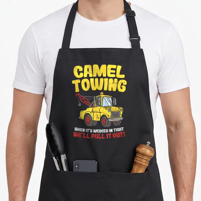 Camel truck apron - Distressed yellow tow truck with CAMEL TOWING text and red hook — shown on a black cotton canvas apron against a white background