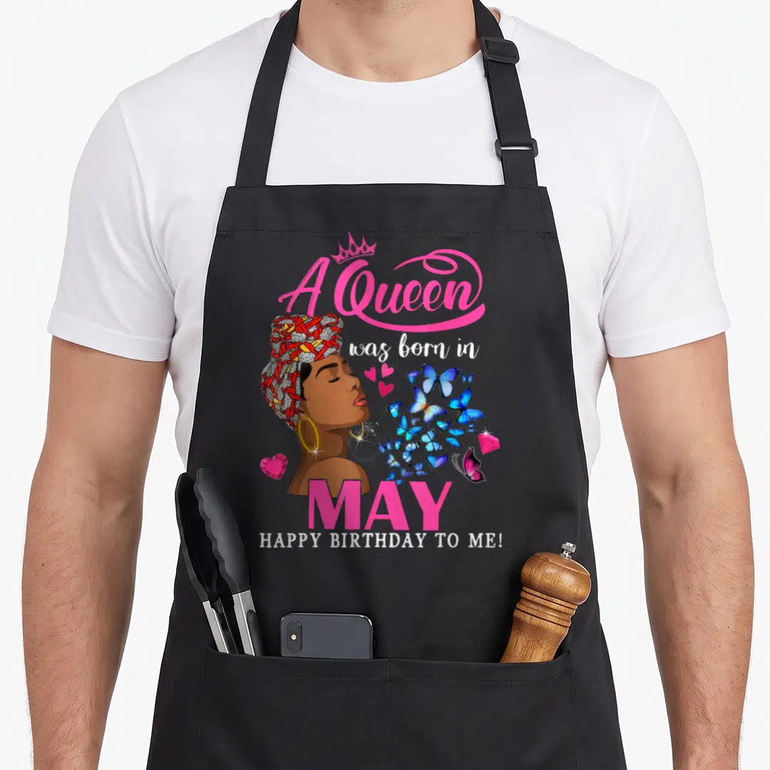 Funny queen may birthday apron - A Queen was born in May cartoon woman with blue butterflies and pink text — shown on a black cotton canvas apron against a white background