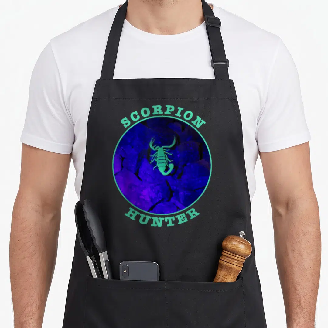 Scorpion hunter apron - Circular photo of a glowing green scorpion on purple rocks with SCORPION HUNTER text — shown on a black cotton canvas apron against a white background