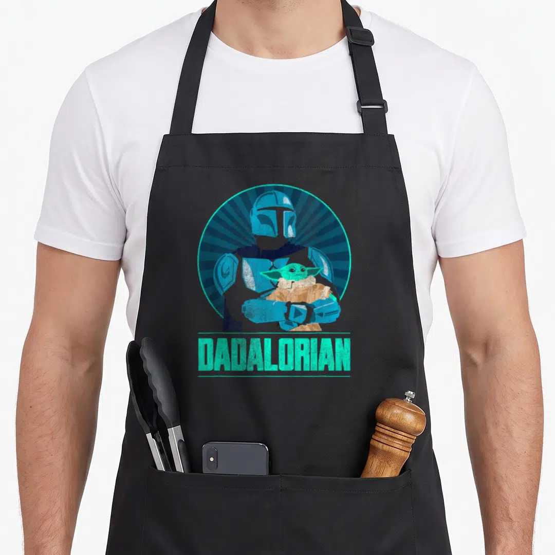 Funny dadalorian father day apron - Cartoon Mandalorian holding Grogu in blue and tan circle above teal Dadalorian text — shown on a black cotton canvas apron against a white background