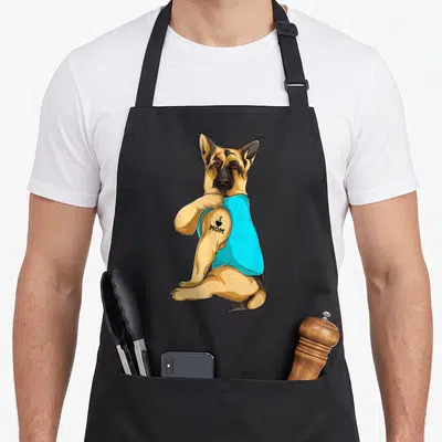 Tattoo dog mom apron - Sitting German Shepherd in cyan tank top with I heart MOM tattoo on bicep — shown on a black cotton canvas apron against a white background