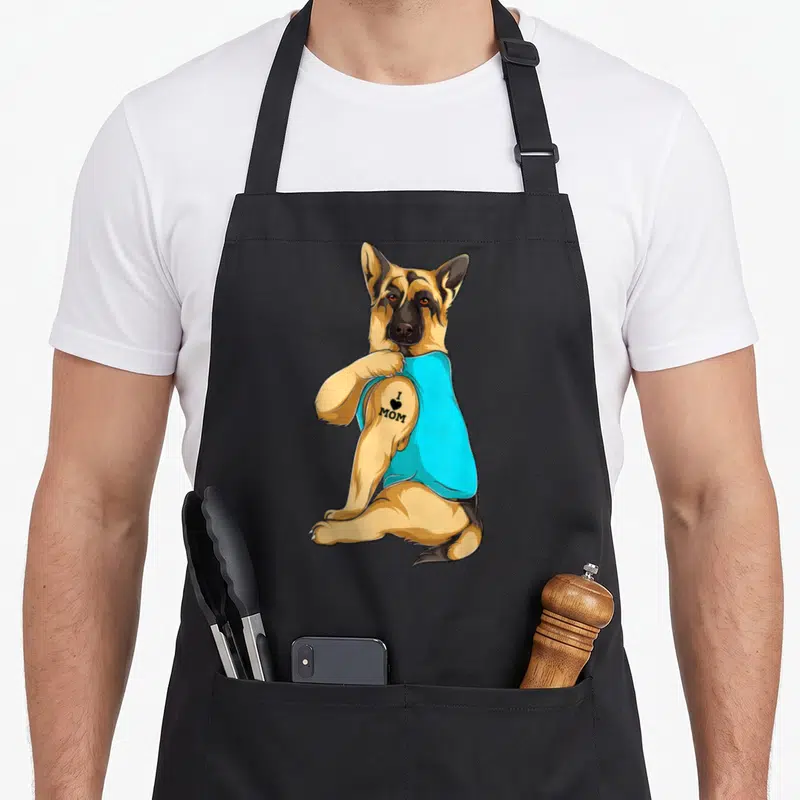 Tattoo dog mom apron - Sitting German Shepherd in cyan tank top with I heart MOM tattoo on bicep — shown on a black cotton canvas apron against a white background