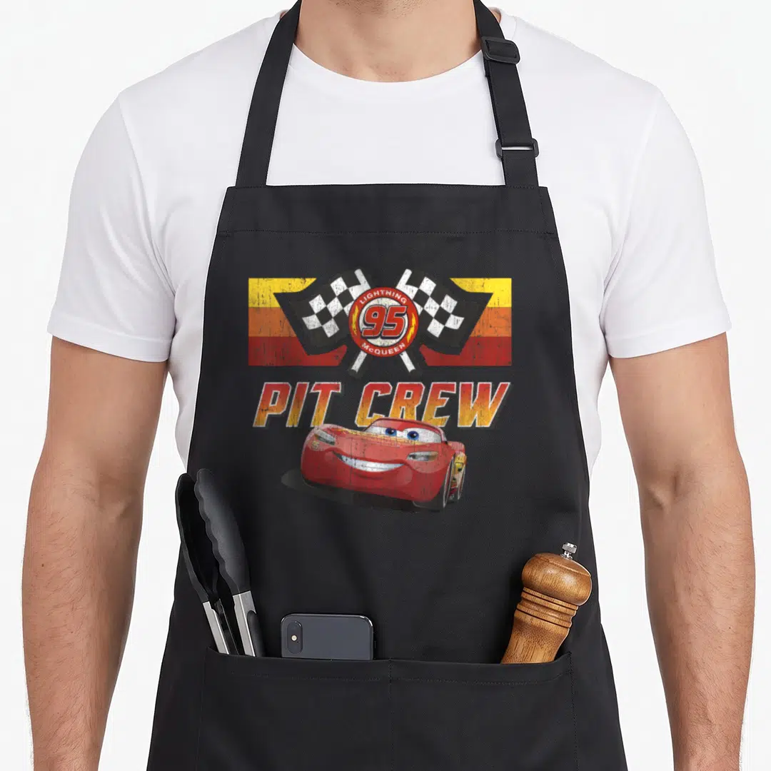 Mcqueen car apron - Red race car, crossed checkered flags, PIT CREW text, and horizontal stripes — shown on a black cotton canvas apron against a white background