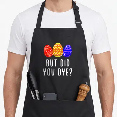 But egg apron - Three red yellow and blue Easter eggs above white text reading But Did You Dye — shown on a black cotton canvas apron against a white background