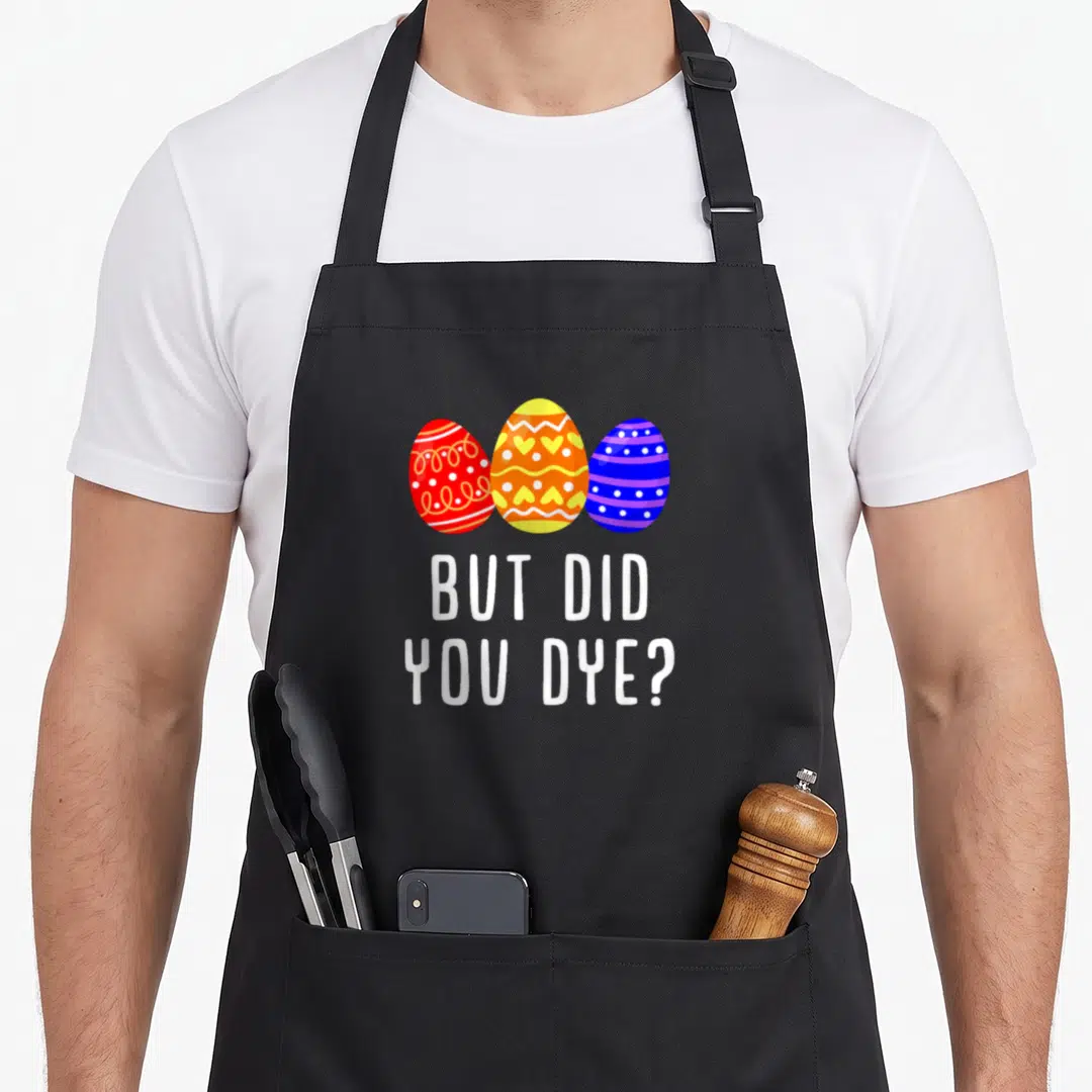 But egg apron - Three red yellow and blue Easter eggs above white text reading But Did You Dye — shown on a black cotton canvas apron against a white background