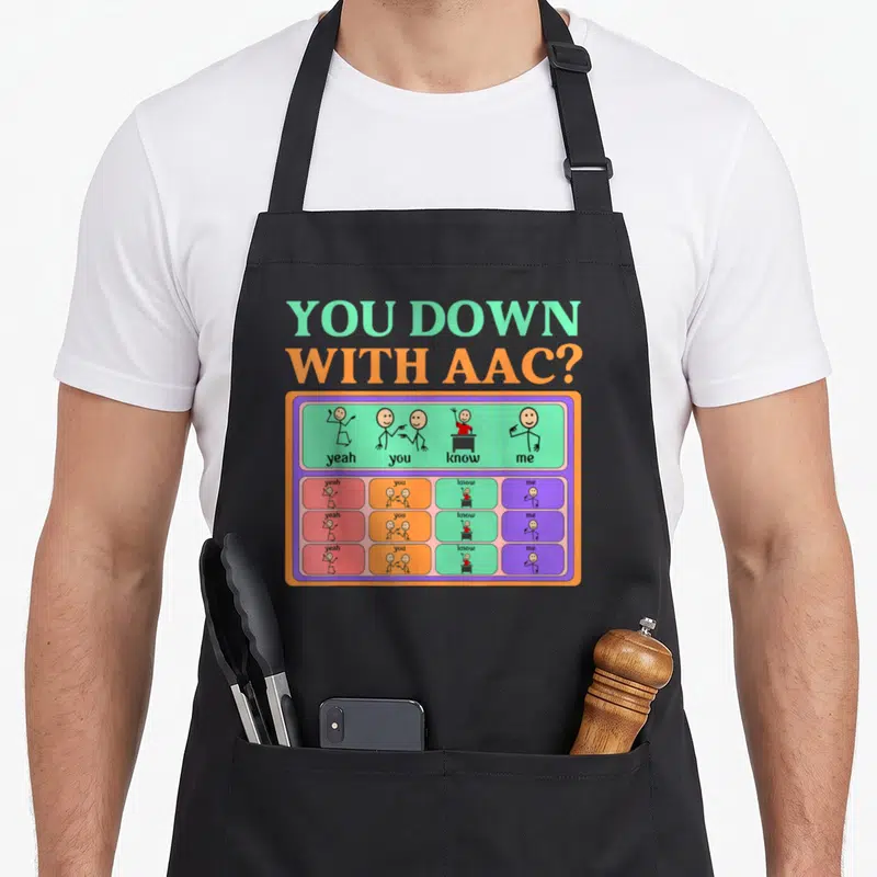 Awareness aac apron - You Down With AAC text above colorful communication board with stick figure icons and three rows — shown on a black cotton canvas apron against a white background