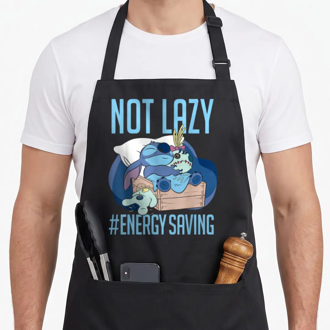 Lazy novelty apron - Blue Stitch hugging plush toy in box with NOT LAZY text — shown on a black cotton canvas apron against a white background