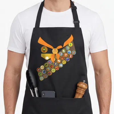 Wilderness halloween apron - Brown sash with circular badges and orange neckerchief knot featuring W E logos — shown on a black cotton canvas apron against a white background