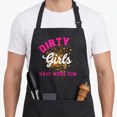 Run the dirty apron - Pink and white text reading DIRTY Girls HAVE MORE FUN over a gold paint splatter on grey — shown on a black cotton canvas apron against a white background