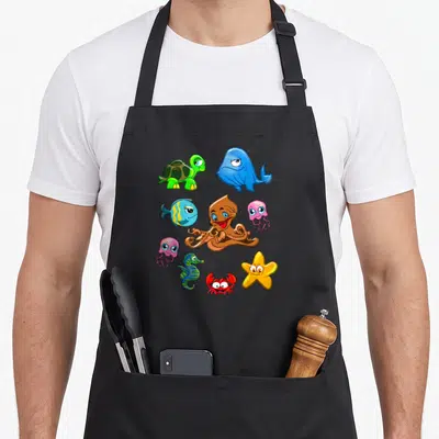 Whale crab apron - Cartoon brown octopus, blue whale, green turtle, pink jellyfish, red crab, and yellow starfish — shown on a black cotton canvas apron against a white background