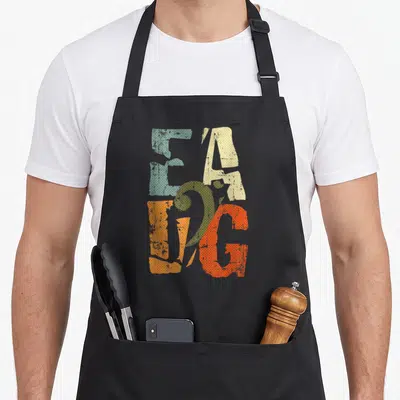 Eadg bassist apron - Stacked EAGLE letters in blue-grey, beige, orange-red, and orange with retro halftone texture — shown on a black cotton canvas apron against a white background