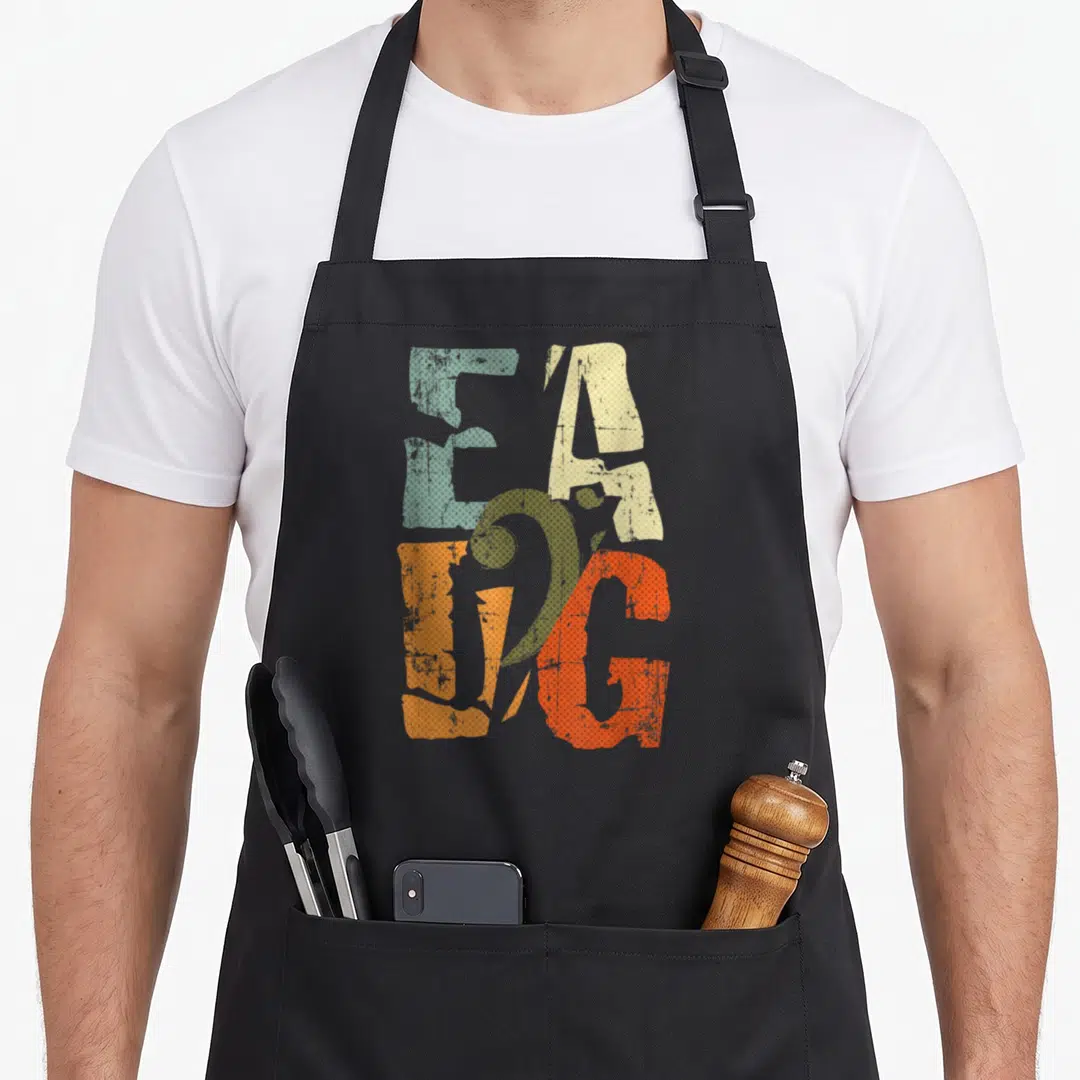 Eadg bassist apron - Stacked EAGLE letters in blue-grey, beige, orange-red, and orange with retro halftone texture — shown on a black cotton canvas apron against a white background