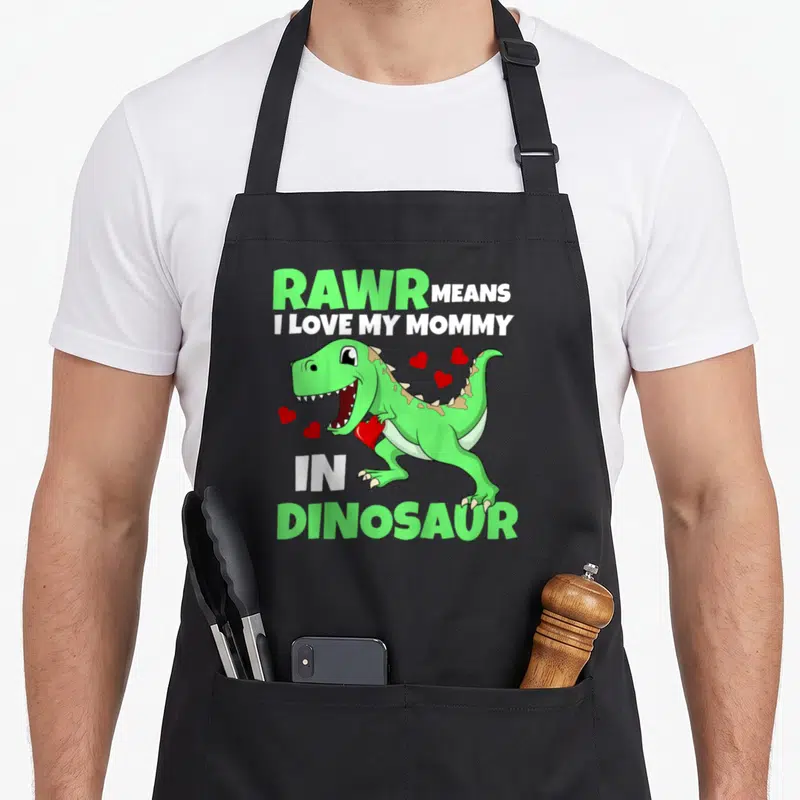 Rawr mother's day aprons - Green cartoon dinosaur holding red heart with text RAWR MEANS I LOVE MY MOMMY IN DINOSAUR — shown on a black cotton canvas apron against a white background