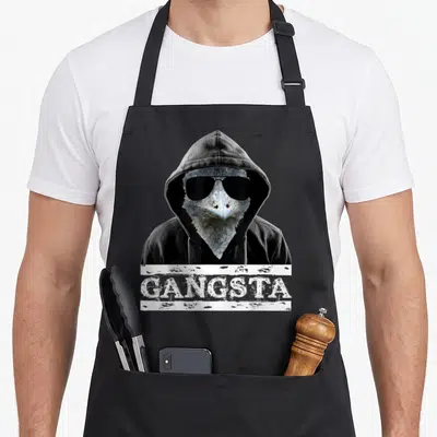 Gangsta bird apron - Raven in black hoodie and sunglasses with white distressed GANGSTA banner — shown on a black cotton canvas apron against a white background