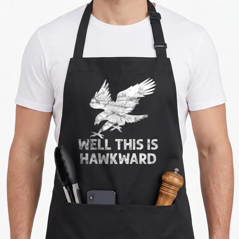 Well bird apron - Distressed white hawk above stacked text reading well this is hawkward — shown on a black cotton canvas apron against a white background