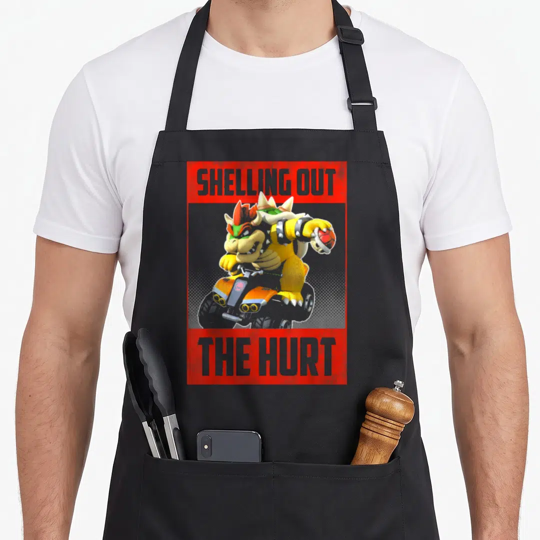 Shelling karting apron - Bowser on kart flanked by red text blocks reading SHELLING OUT THE HURT — shown on a black cotton canvas apron against a white background