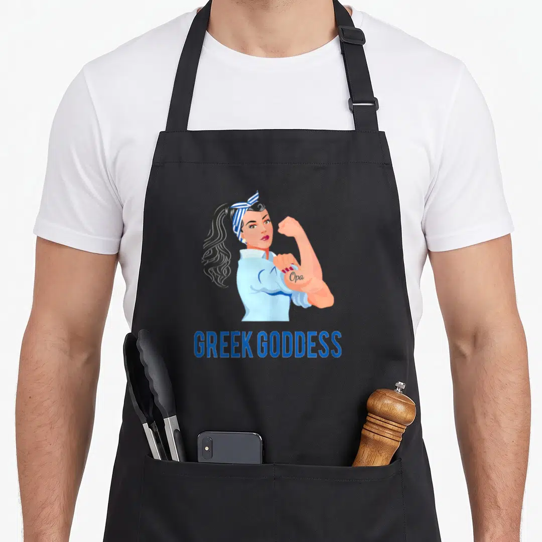 Strong greek aprons - Cartoon woman flexing bicep with Opa tattoo and Greek Goddess text in blue white red — shown on a black cotton canvas apron against a white background