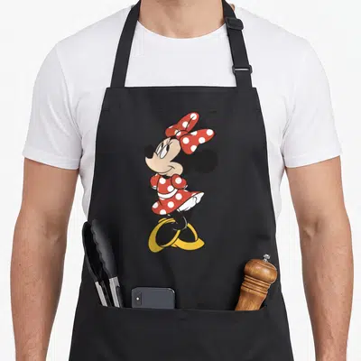 Traditional portrait friends apron - Minnie Mouse standing in red polka dot dress with yellow shoes — shown on a black cotton canvas apron against a white background