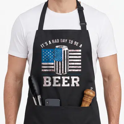 Cute beer apron - Distressed beer can with US flag stripes and arched text IT'S A BAD DAY TO BE A BEER — shown on a black cotton canvas apron against a white background
