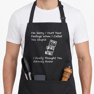 Sorry stupid aprons - White line-art robot of stacked cubes with sarcastic apology text — shown on a black cotton canvas apron against a white background