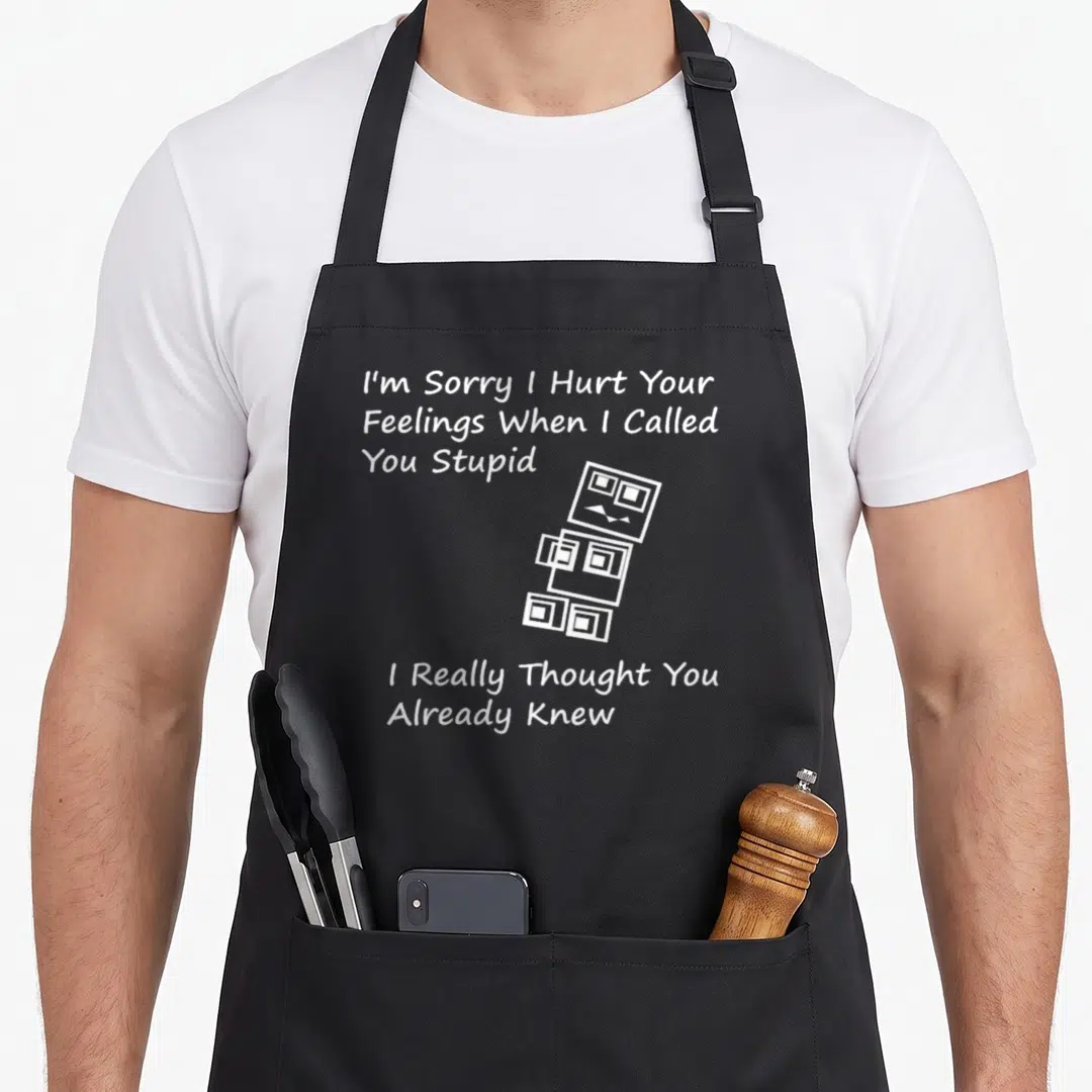 Sorry stupid aprons - White line-art robot of stacked cubes with sarcastic apology text — shown on a black cotton canvas apron against a white background