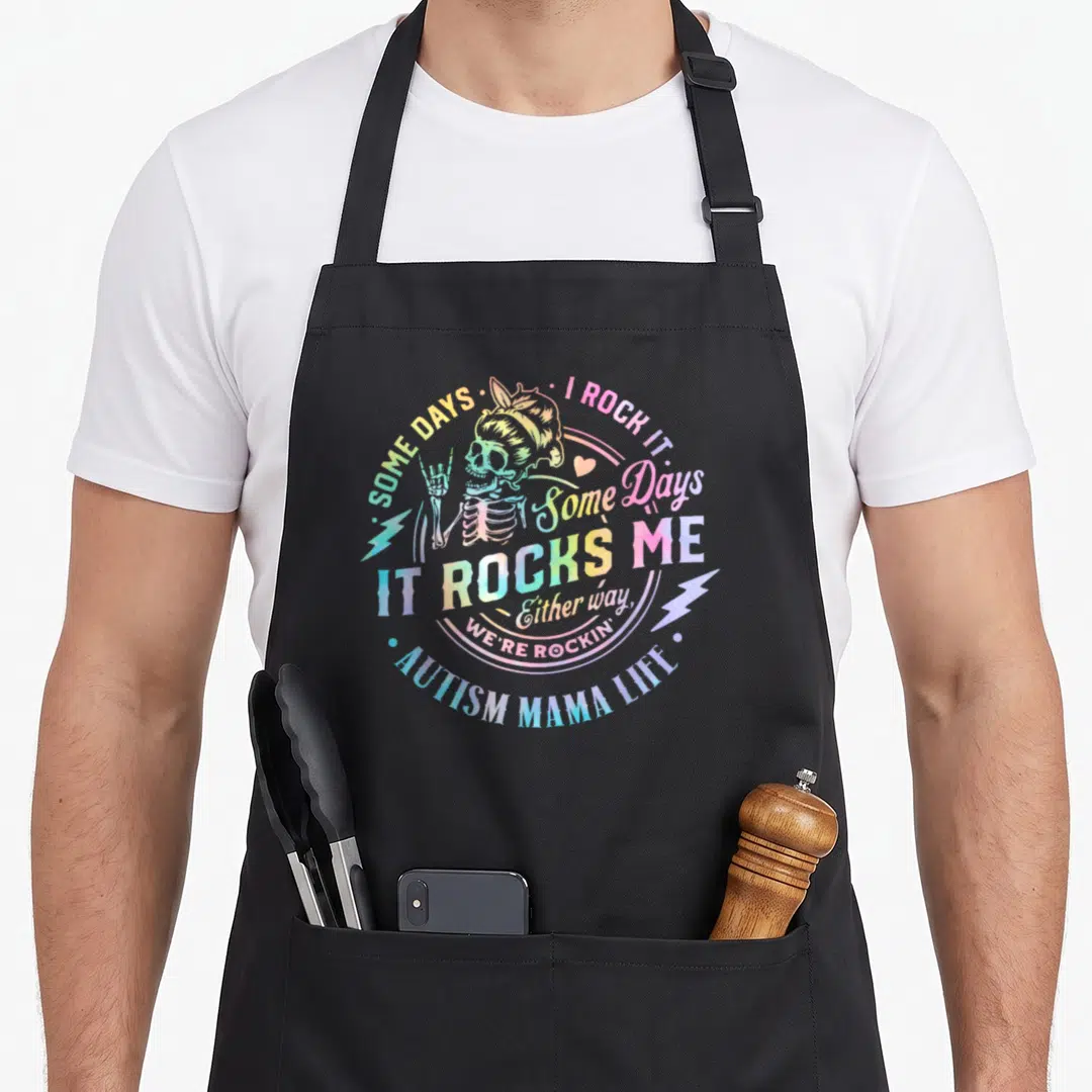Rock mama apron - Distressed skeleton making rock sign surrounded by rainbow text about autism mama life — shown on a black cotton canvas apron against a white background