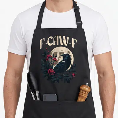 Caw meme apron - Retro black crow perched on red roses and leaves under arched F-CAW-F text against a beige moon — shown on a black cotton canvas apron against a white background