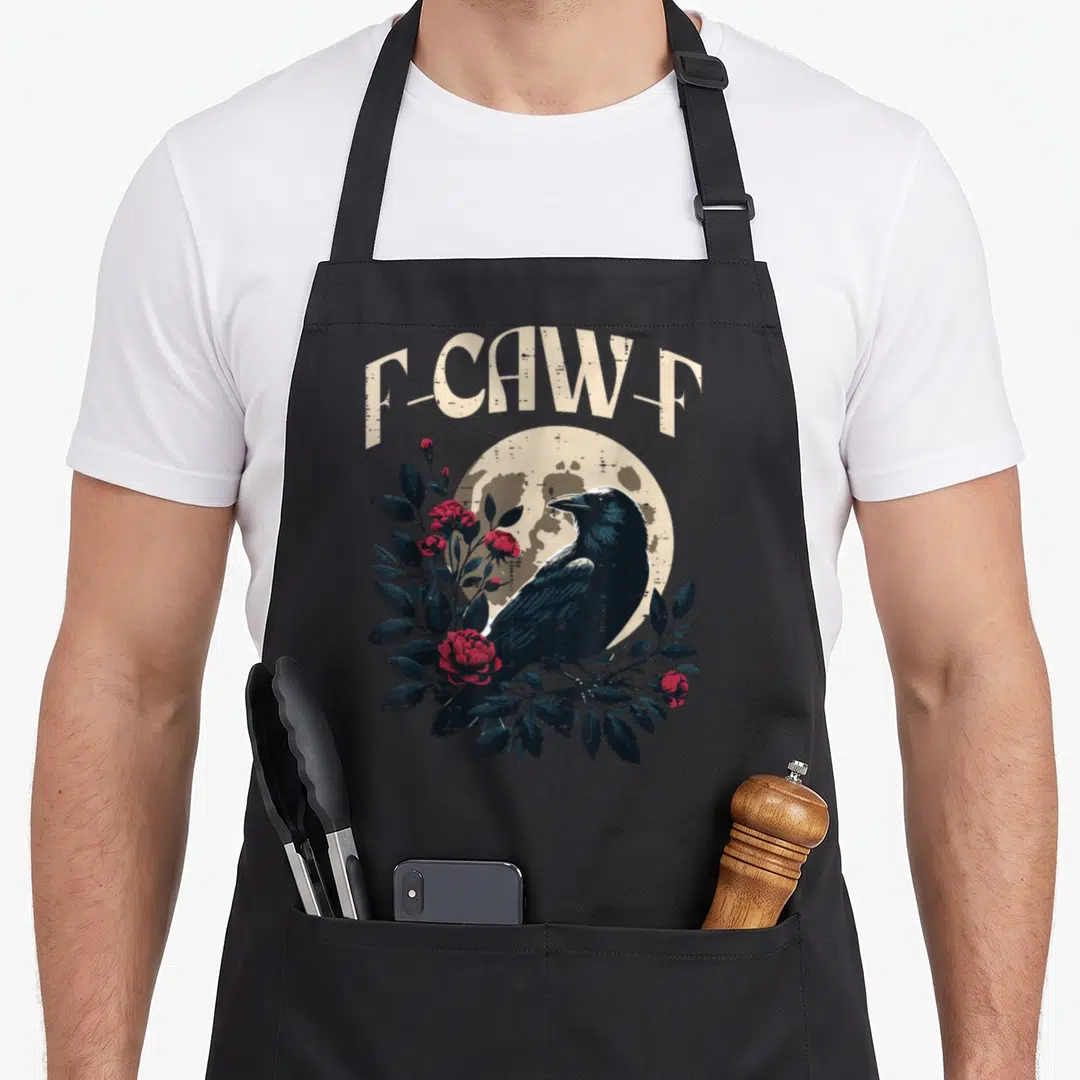 Caw meme apron - Retro black crow perched on red roses and leaves under arched F-CAW-F text against a beige moon — shown on a black cotton canvas apron against a white background