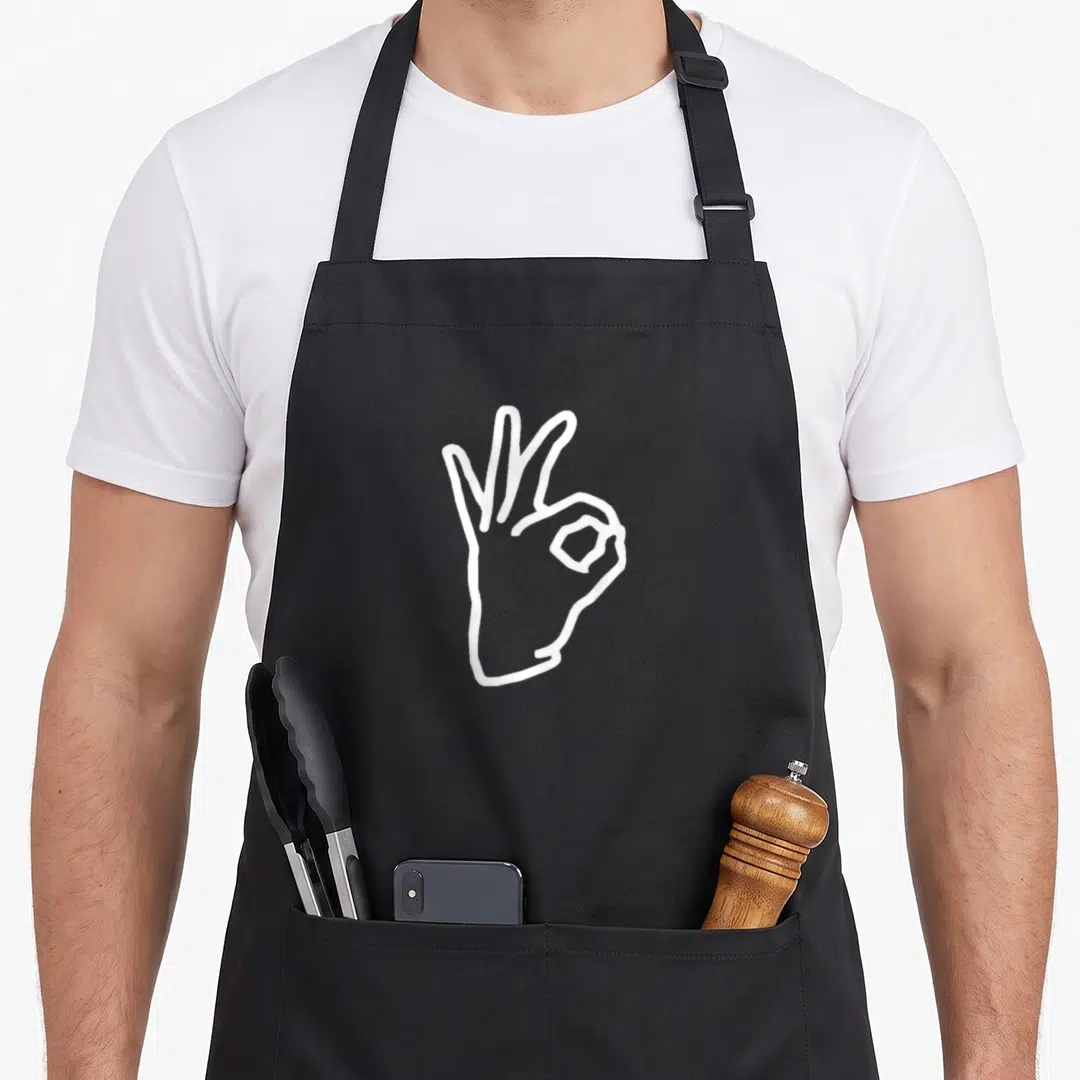 Boredkoalas meme apron - White line art hand making ok sign on black bib apron — shown on a black cotton canvas apron against a white background