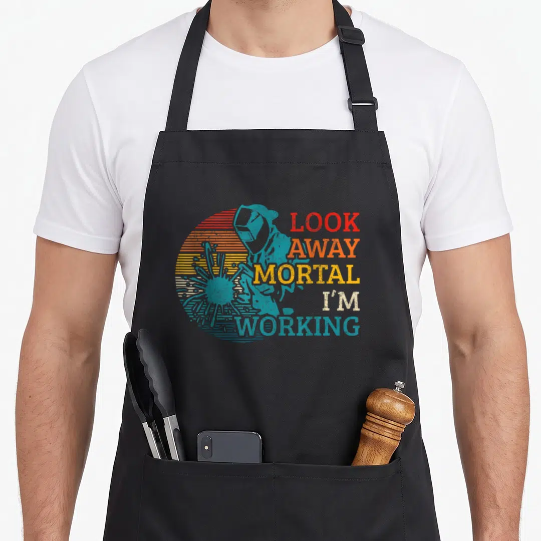 Welding locksmith apron - Retro blue welder silhouette over striped sun with text LOOK AWAY MORTAL I'M WORKING — shown on a black cotton canvas apron against a white background