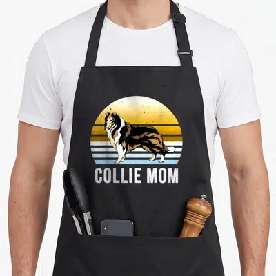 Cute rough dog apron - Retro standing collie on striped sun background with white text reading COLLIE MOM below — shown on a black cotton canvas apron against a white background