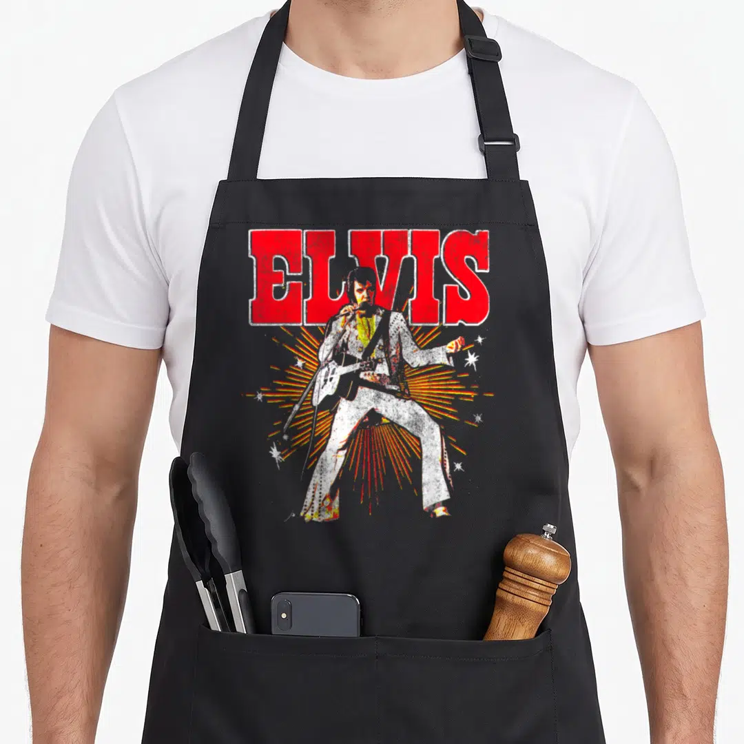 Elvis big band apron - Red ELVIS text above a white guitarist figure with yellow and red sunburst rays — shown on a black cotton canvas apron against a white background