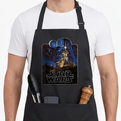 Epic new hope apron - Vintage Star Wars poster print with blue Vader helmet, Luke, Leia, droids, and TIE fighters — shown on a black cotton canvas apron against a white background