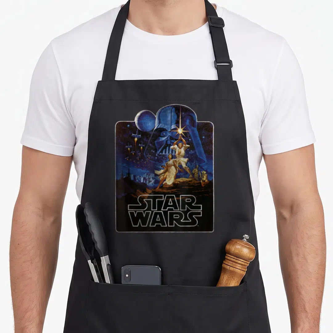 Epic new hope apron - Vintage Star Wars poster print with blue Vader helmet, Luke, Leia, droids, and TIE fighters — shown on a black cotton canvas apron against a white background