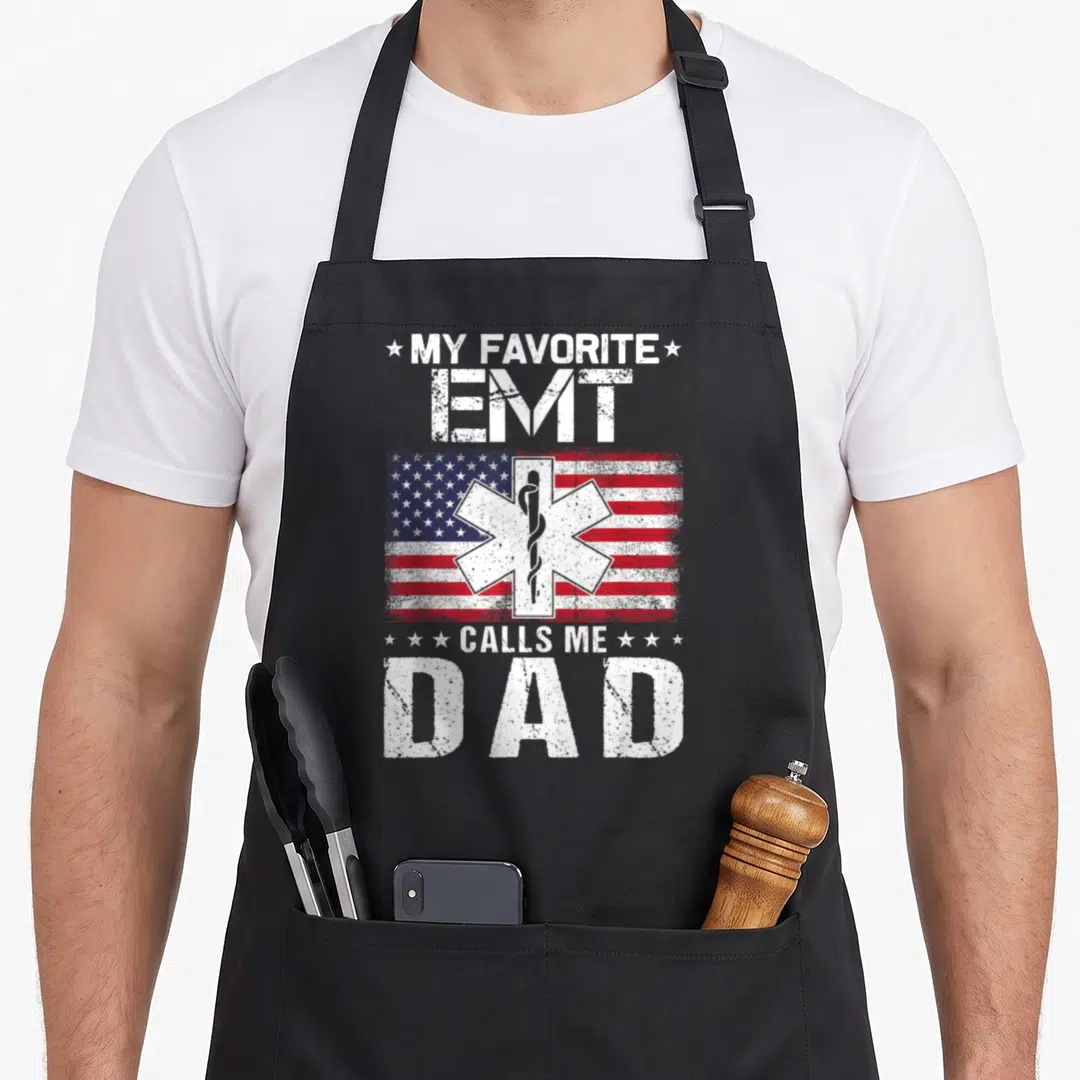 Emt father day apron - My Favorite EMT Calls Me Dad text over distressed US flag and white Star of Life symbol — shown on a black cotton canvas apron against a white background